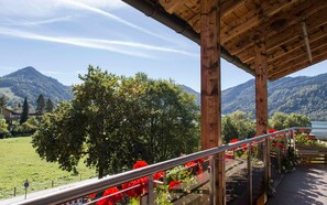 Un balcon en bois, doté d’une rambarde en métal, offre une vue sur un paysage montagneux avec un lac.