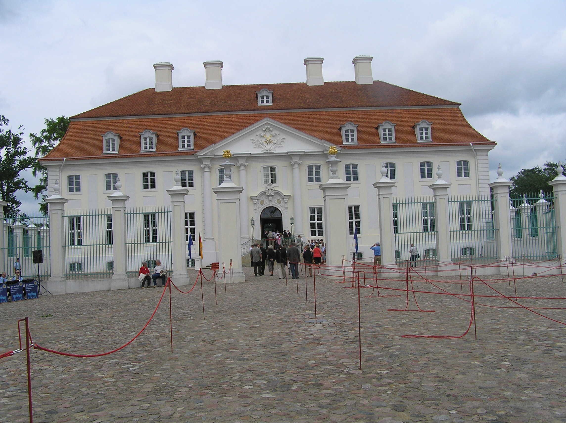 Un bâtiment historique à la façade symétrique, doté d’une entrée centrale et d’une cour dallée.