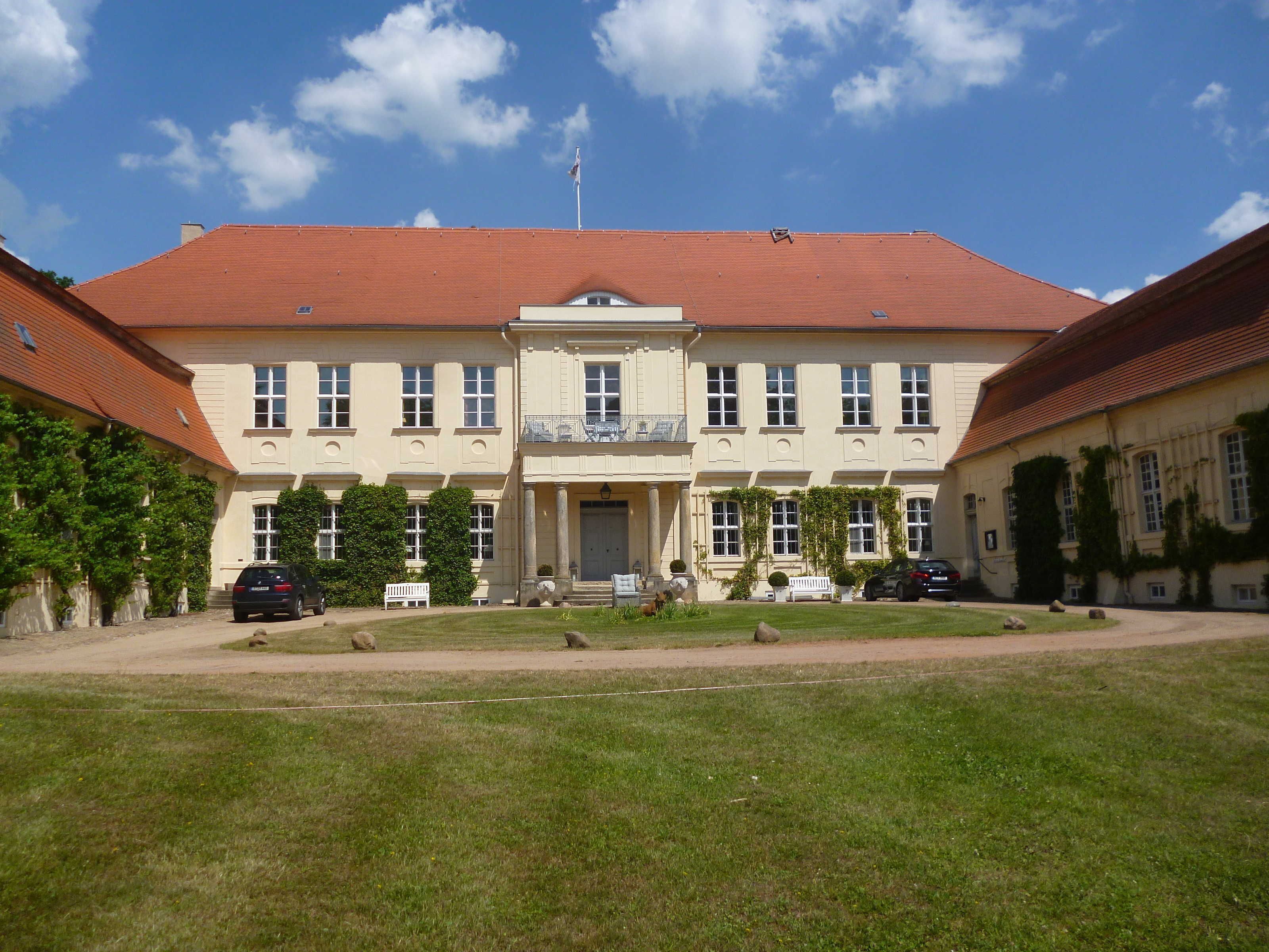 Ein großes, symmetrisches Gebäude mit einem zentralen Eingang, zahlreichen Fenstern und einem roten Ziegeldach.