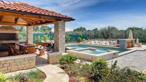 Un patio trasero con una parrilla de piedra, una piscina y una pérgola.