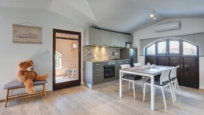 Una cocina moderna con armarios grises, una mesa de comedor con sillas blancas y un osito de peluche en un banco.