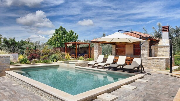 Piscina con sillas de descanso, una pérgola y zona de barbacoa.