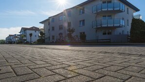 A multi-story building with a flat roof, balconies, and a paved ground.