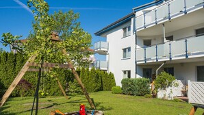A modern apartment building with a balcony and a swing set in the yard.