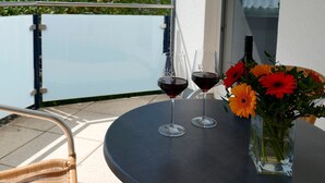 A balcony with a table, two wine glasses, and a vase with flowers.