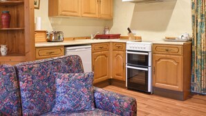 Une cuisine avec des meubles en bois, une cuisinière, un lave-vaisselle et un coin repas agrémenté d’un canapé à motifs.