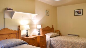 Une chambre avec deux lits, des tables de chevet avec des lampes, une étagère avec des livres et un radiateur.