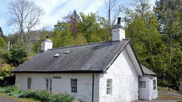 Un bâtiment en pierre blanche, doté d’un toit à deux versants, d’une cheminée et d’une petite structure adjacente.