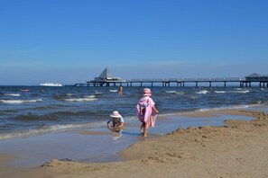 Une plage avec une jetée qui s’avance dans l’eau, un bateau et des personnes près du rivage.