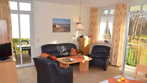 Una sala de estar con un sofá, un sillón y una mesa con un frutero.