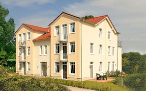 Un immeuble à plusieurs étages doté de balcons, d’un toit recouvert de tuiles rouges et d’un espace jardin avec des sièges extérieurs.