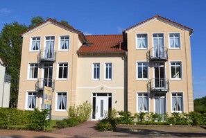 A two-story building with balconies, a central entrance, and a clear sky.