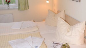 Una cama bien hecha con almohadas y una colcha, una lámpara de noche, un cuadro en la pared y una ventana con cortina.