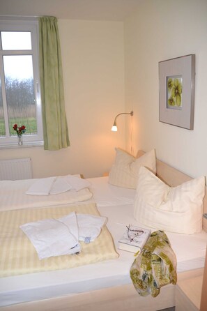 A neatly made bed with pillows and a blanket, a bedside lamp, a framed picture on the wall, and a window with a curtain.