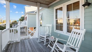 A covered porch with white rocking chairs and a small table, overlooking a residential area. - Night N Gale-Close to Beach Access in Atlantic Beach, NC (Atlantic Beach)