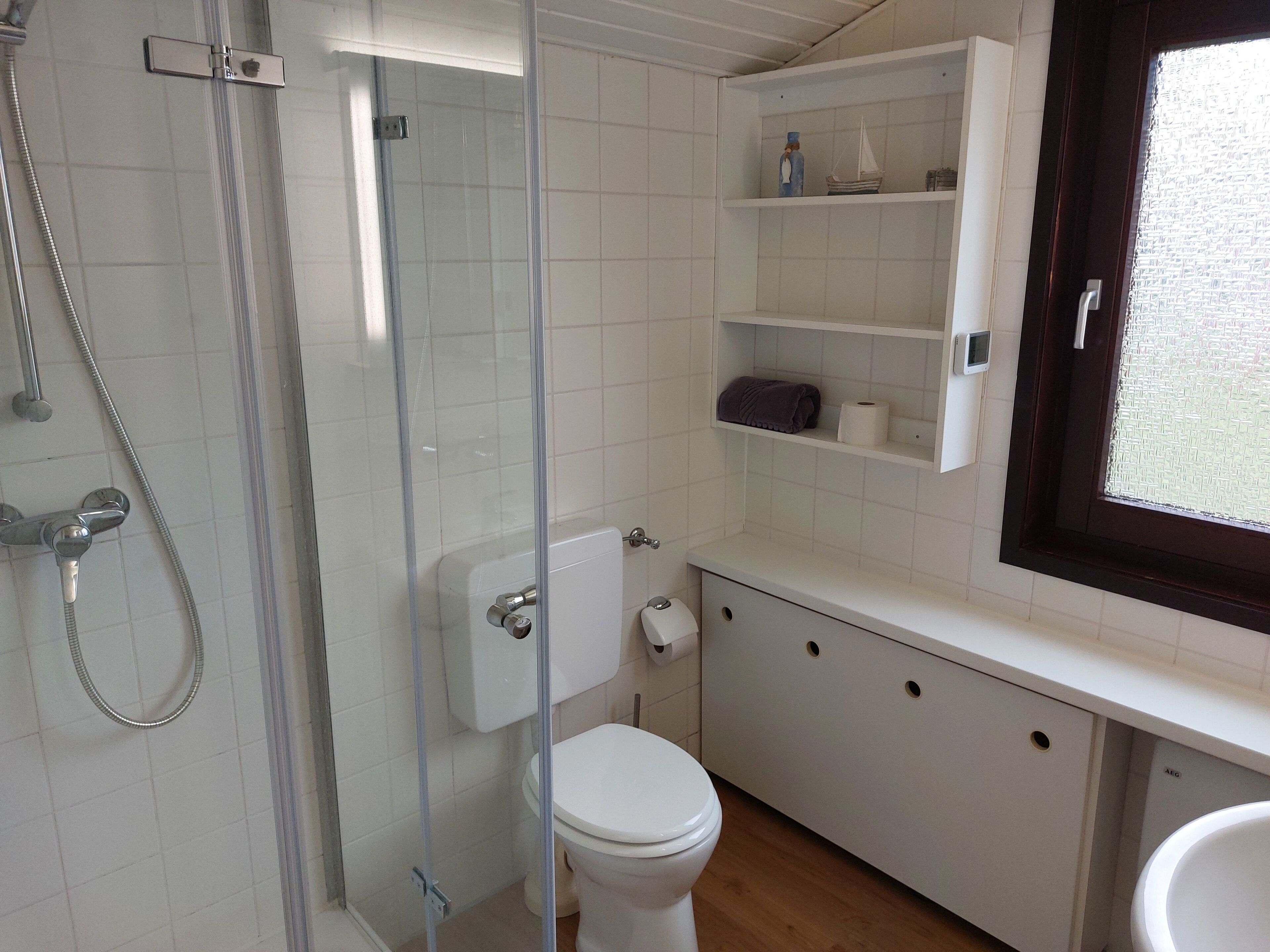 A bathroom with a glass-enclosed shower, a toilet, a sink, and a window.