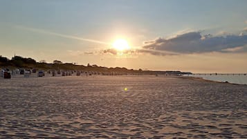A beach with a sunset, a pier, and beach huts.