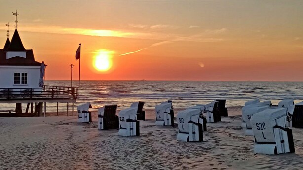 Ein Gebäude direkt am Strand mit einer Flagge, einem Steg und Liegen mit Preisen.