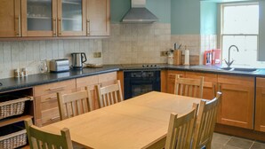 A kitchen with wooden cabinets, a stainless steel range hood, a built-in oven, a sink, and a dining table with chairs. - Tressady Coach House (Rogart, near Dornoch)