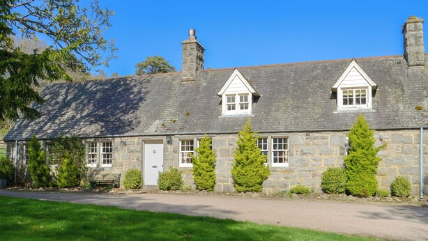 A stone cottage with a white door, two chimneys, and a small porch. - Tressady Coach House (Rogart, near Dornoch)