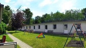 Une zone herbeuse avec des jeux pour enfants, une table de pique-nique et un bâtiment doté de fenêtres.