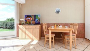 Un comedor con una mesa y sillas de madera, un televisor en un mueble y un reloj en la pared.