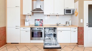 Una cocina compacta con armarios blancos, microondas, lavavajillas y estufa.