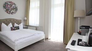 A hotel room with a bed, a desk with a lamp, a coffee maker, and a television. - Double room *** - Aparthotel Waldfrieden (Sellin)
