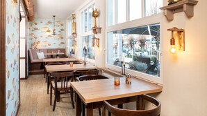 A restaurant with wooden tables and chairs, a bench seating area, and large windows with views of the street. - Double room *** - Aparthotel Waldfrieden (Sellin)