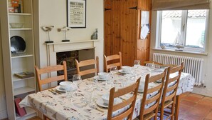 Comedor con mesa dispuesta para seis comensales, sillas de madera, chimenea, estantería y ventana con vistas.