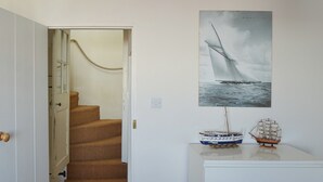 Una escalera conduce a una habitación con un cartel de un barco de vela, un pequeño modelo de barco y un armario blanco.