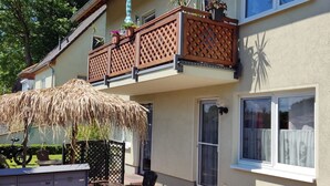 Un edificio de dos pisos con un balcón, un toldo de paja y una pequeña zona de estar al aire libre.