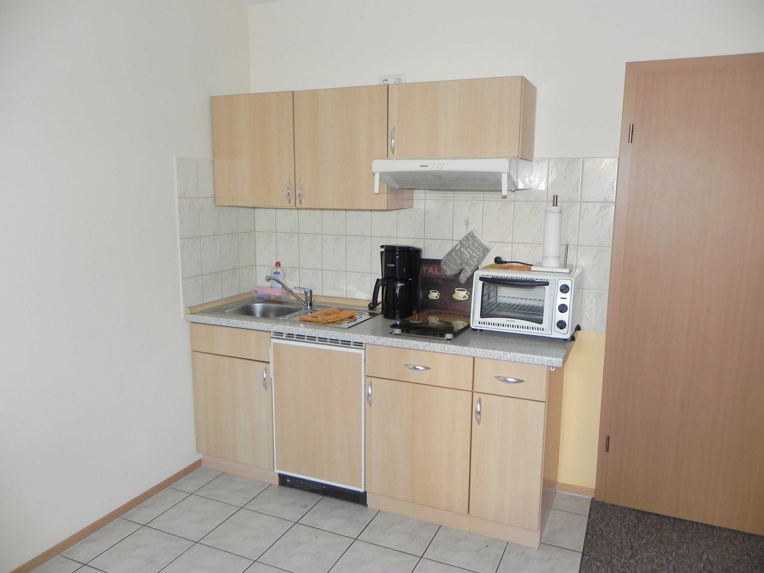 A small kitchen with wooden cabinets, a Bosch oven, a coffee maker, and a sink.