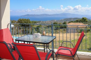 A balcony with a glass table and red chairs, overlooking a scenic view of the sea and hills. - ANGIO VILLAS SPA WITH HYDROTHERAPY POOL (Skiathos)