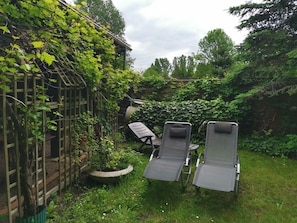 A garden with a wooden trellis, two lounge chairs, and a stone planter. - Sleeping in the hay / hay bed - Ferienhof Sarodnick (Lauta)