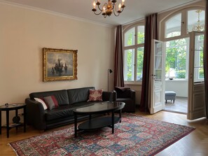 Un soggiorno con un divano nero, un tavolino da caffè, un tappeto decorato, un quadro incorniciato e ampie finestre con tende.