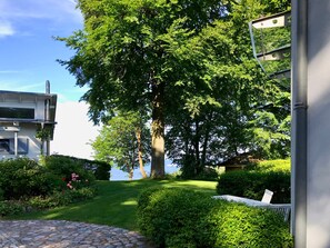 A garden with a large tree, a stone pathway, and a building with a modern design. - Apartment III: Ground floor South & Sea - Villa Achterkerke (Heringsdorf)