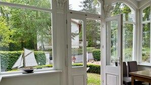 A conservatory with a sailboat model, a dining area with chairs, and a patterned floor. - Apartment III: Ground floor South & Sea - Villa Achterkerke (Heringsdorf)