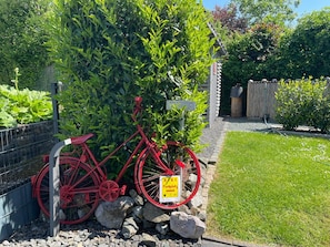 A red bicycle parked against a hedge, a sign indicating a private parking area, and a grassy lawn.