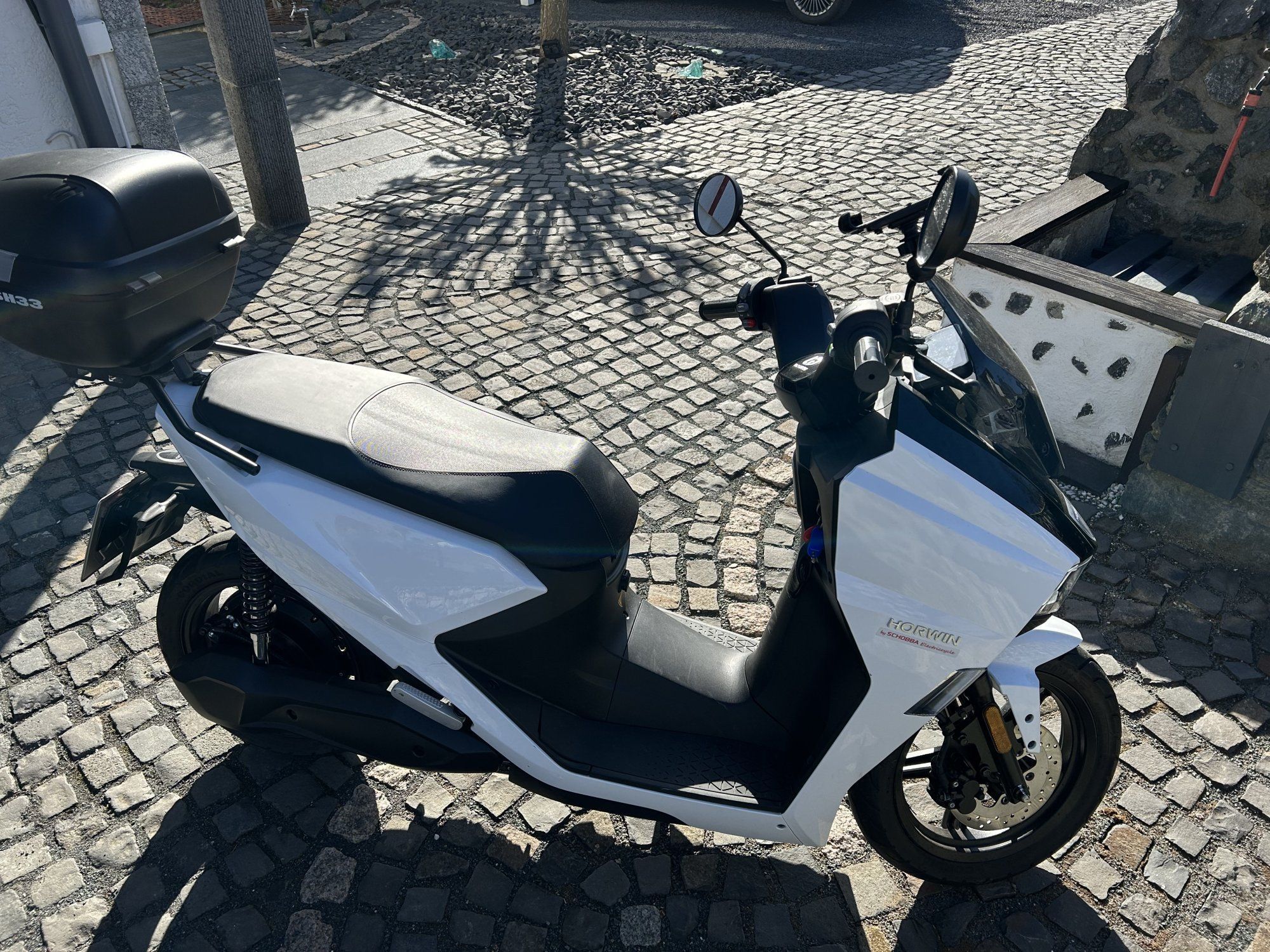 Ein schwarz-weißer Roller steht auf einer Kopfsteinpflasterstraße.