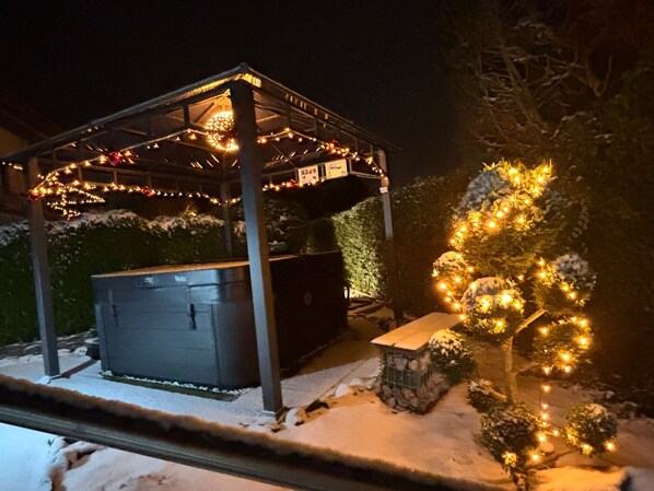 Un espacio al aire libre techado con un jacuzzi, suelo cubierto de nieve y luces colgantes.