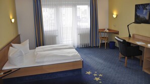 A hotel room with a bed, desk, chair, and a painting on the wall.