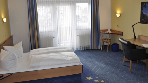 A hotel room with a bed, a desk, a chair, and a lamp.