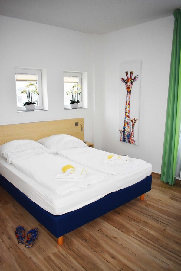 A bedroom with a bed, two windows with plants, a giraffe painting, and a green curtain.