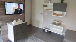 Una sala moderna con una televisión de pantalla plana, un mostrador de recepción, estanterías empotradas y un sofá gris.