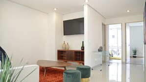 Ein modernes Wohnzimmer mit einem flachbildfernseher an der Wand, einer Holzkommode mit Dekoration und einem Glastisch.