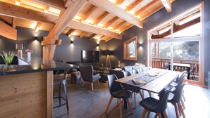 A spacious dining area with a long wooden table and modern chairs, a cozy seating area with a sofa and chairs, and a large window providing a view of the outdoors. - Super endroit ! Chalet montagnard avec sauna (L'Alpe d'Huez)