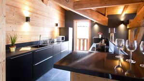 A modern kitchen with wooden beams, a black countertop, and a view of the dining area. - Super endroit ! Chalet montagnard avec sauna (L'Alpe d'Huez)