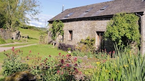 A stone building with a sloped roof, a garden with various plants, and a wooden fence.