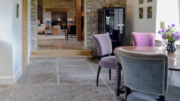 A stone archway leading to a living room with a fireplace, a dining table with chairs, and a refrigerator.